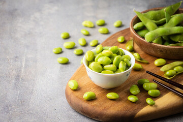 Top view of bowl with grains and edamame pods with toothpicks on wooden table, gray background, horizontal