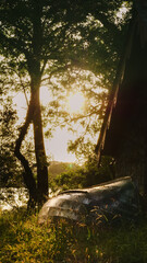 Obraz premium Boat at the rear of an abandoned boat house as the sun begins to set in the background through the trees