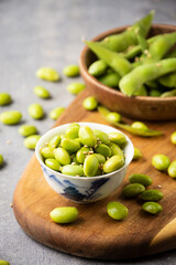 Top view of bowl with grains and edamame pods with sesame on wooden board, selective focus, gray background, vertical