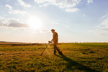 Treasure hunter stands against the blue sky. Treasure hunter holding a modern metal detector. Guy with a shovel looking for treasure