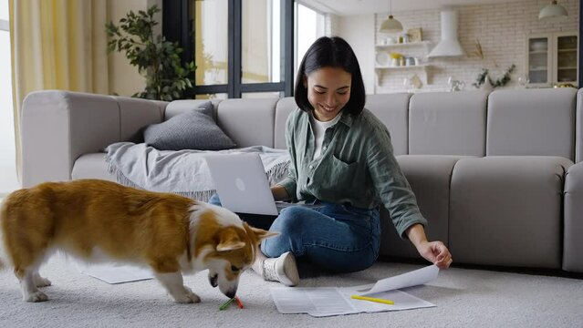 Asian woman works on computer and gives dog treats smiling