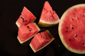 Top view of watermelon slices and halved watermelon on black surface