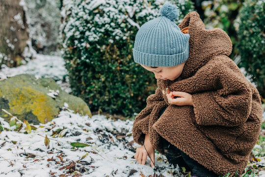 Little Kid In Hat And Coat In Winter Snowy Garden