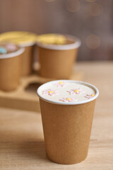 a paper cup with cake to go with cream drawing flowers on a table and three homemade mini chocolate cake in coffee cups in a box on background, confectionery trend concept. Vertical, copy space, Bokeh