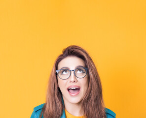 Surprised young woman looking up to free space - copy space for your product or text, wearing blue leather jacket, isolated on yellow background