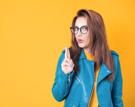 Young woman doing gun gesture getting ready to shoot, cute girl showing gun gesture, wearing blue leather jacket, isolated on yellow background