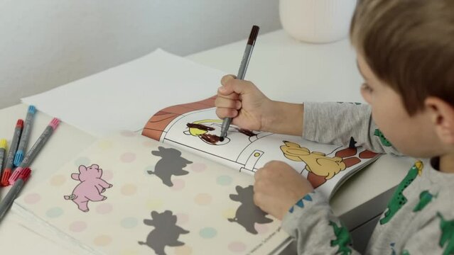 A little boy paints pictures with markers at home on the table