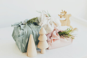 Zero waste Christmas. Stylish wrapped gifts in linen fabric on white rustic table with eco wooden tree, deer, fir branches. Furoshiki gift wrapping. Eco friendly toys. Merry Christmas!
