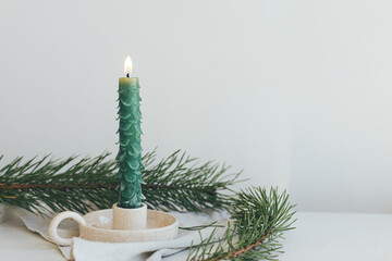 Stylish christmas candle as fir tree on white rustic table with fir branches and linen cloth....