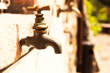 Bronze old iron water tap, without water, closed outdoor, on the stone wall, in hot sunny day, with...