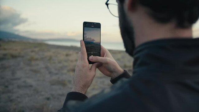 Man shooting video with his smart phone on the beach near the ocean