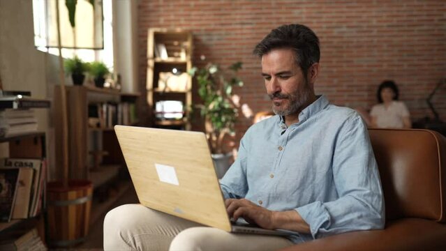 Middle aged hispanic couple teleworking and sharing their day at home. Focus on caucasian man with laptop