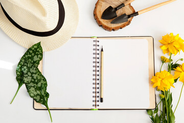 Floral Gardening mockup with an assortment of garden flowers, garden hat,  blank paper notebook, pencil and gardening tools, top view, frame.