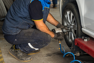 Auto mechanic man with electric screwdriver changing tire outside. Car service. Tire installation concept.