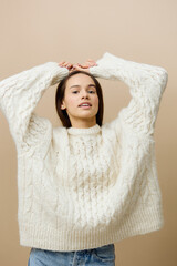 an elegant woman stands on a light background in a white sweater, raises her hands over her naked, puts them behind her back and turns her body in different directions