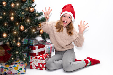 happiness concept, cute girl near the christmas tree holding a gift. happy child on a white background in a red New Year's hat  plays and shows funny faces.