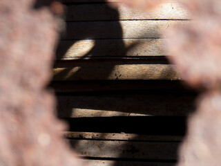 A rustic wooden wall seen through the hole of a rusted metalic plate, captured in a farm near the...