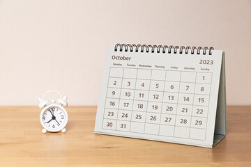 October 2023 calendar and small alarm clock on a wooden table