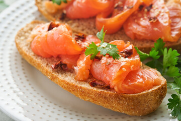 Sandwiches with salted salmon. Open sandwiches from cereal or whole grain rye bread with salted salmon, sesame seeds and dried tomato on white marble stand. Seafood. Healthy food. Scandinavian cuisine
