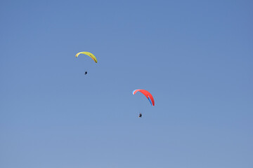 Two flying paragliders in the blue sky.