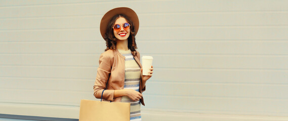 Portrait of beautiful happy smiling woman with shopping bags and cup of coffee wearing jacket, round hat on gray background, blank copy space for advertising text