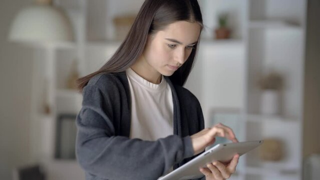 Young freelance designer working from home white modern office using tablet, scrolling the finger on the screen, moving objects and doing project for customers, concept of tele work