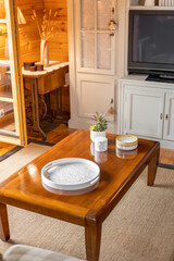 Wooden tea table in living room of the cottage. Decorative tray, candles and a white vase with plants in the interior