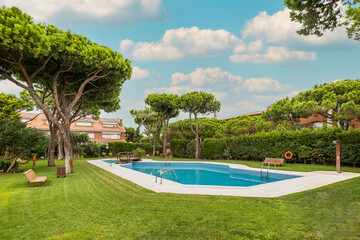 Backyard of residential complex with garden and swimming pool with trees around on sunny day.