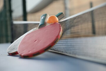 Closeup of a table tennis net with a ball and rackets.