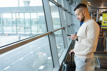 man sits in airport terminal using mobile phone talking via video call.  Airport Terminal: man waiting for flight, using smartphone, browse internet, social Media, online Shopping. 