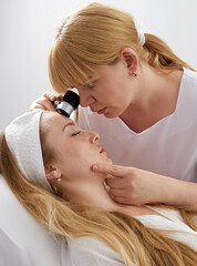 Woman gets professional skin exam at doctor's office. Dermatologist or cosmetology specialist uses...