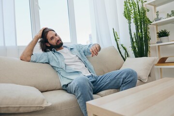 Obraz premium A young male freelancer sits on the couch after a demanding job and rests sadly leaning on the couch. 