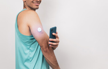 Measurement of blood glucose with the help of mobile applications and sensors. The young man approaches the cell phone to the sensor located in the patch on his arm.