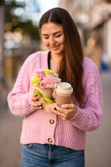 Fototapeta premium pretty woman gently holds flower arrangement in small pot and paper cup of coffee in her hands.