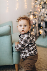 A little curly boy spends time at home near the Christmas tree