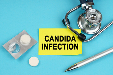 On a blue surface, a stethoscope, pills, a pen and a yellow sticker with the inscription - Candida...