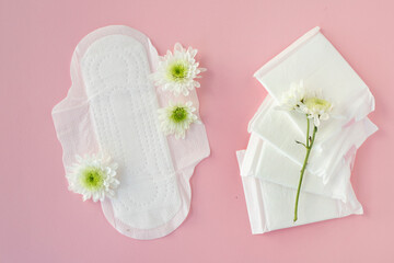 Obraz na płótnie Canvas Sanitary pads and white flowers on pink background. Concept of critical days, menstruation