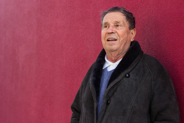 Happy senior man standing against the red wall