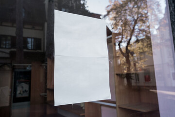 White blank paper sheet sticking with adhesive tape on window glass of store or cafe