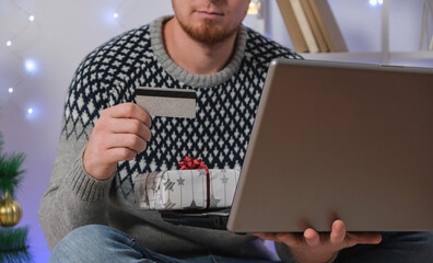 Man with laptop and credit card buys gifts for New Year 2023, Christmas. A man in Santa hat on the...