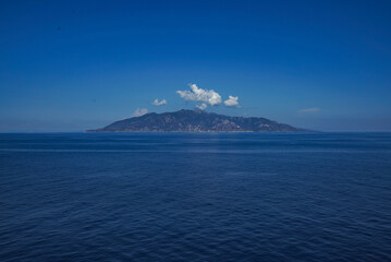 Blue sea and sky, in the distance a mountain on the horizon and a white cloud over the mountain. And nothing else on the water, no people, no ships, just a landscape