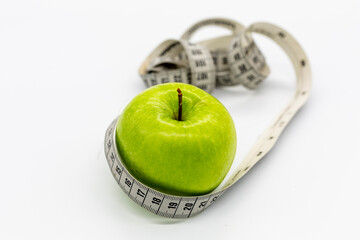 tape measure wrapped around a green apple standing on a white background. Healthy eating and diet food. Weight loss and fitness activities. Vegan diet. Green apple.