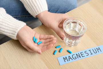 Woman taking magnesium pills at wooden table, closeup