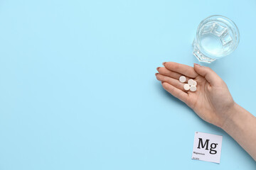 Female hand with magnesium pills and glass of water on blue background