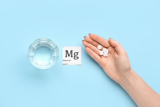 Female hand with magnesium pills and glass of water on blue background