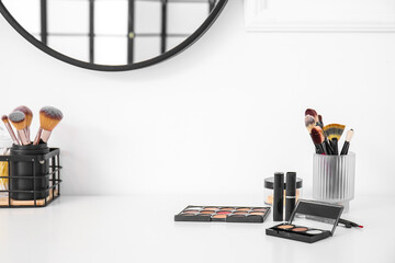 Holder with brushes and decorative cosmetics on white table of makeup artist