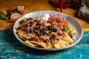 Appetizing plate of nachos with black beans, meat, cheese,sour cream and guacamole on a wooden table