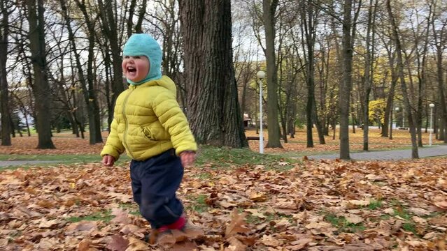 The moment of pure happiness, when toddler is meeting his mother and raising the leaves from the ground by legs. The baby is running to mommy and laughing.