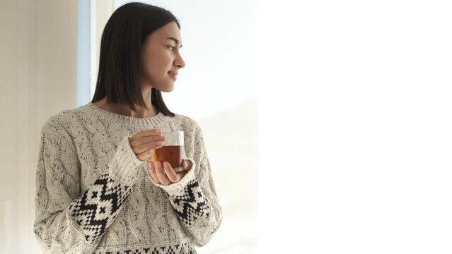 Girl standing thinking by window drinking te. The tranquility of home with the whole family comfortably. Preparing for the day's work and studies.