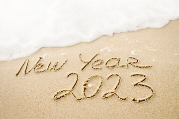 New Year 2023 handwritten lettering on the sandy beach with white foamy ocean wave background. Winter holidays, travel and tropical vacation concept photo